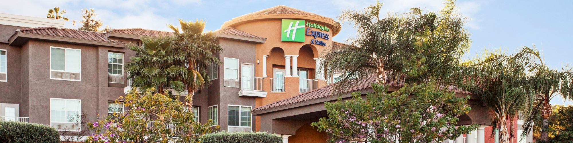 A modern hotel with the Holiday Inn Express logo, surrounded by palm trees and well-maintained landscaping, is pictured on a clear day.