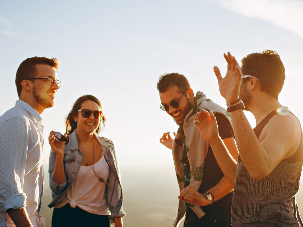 A group of four people enjoying time together outdoors, smiling and gesturing in the sunlight.