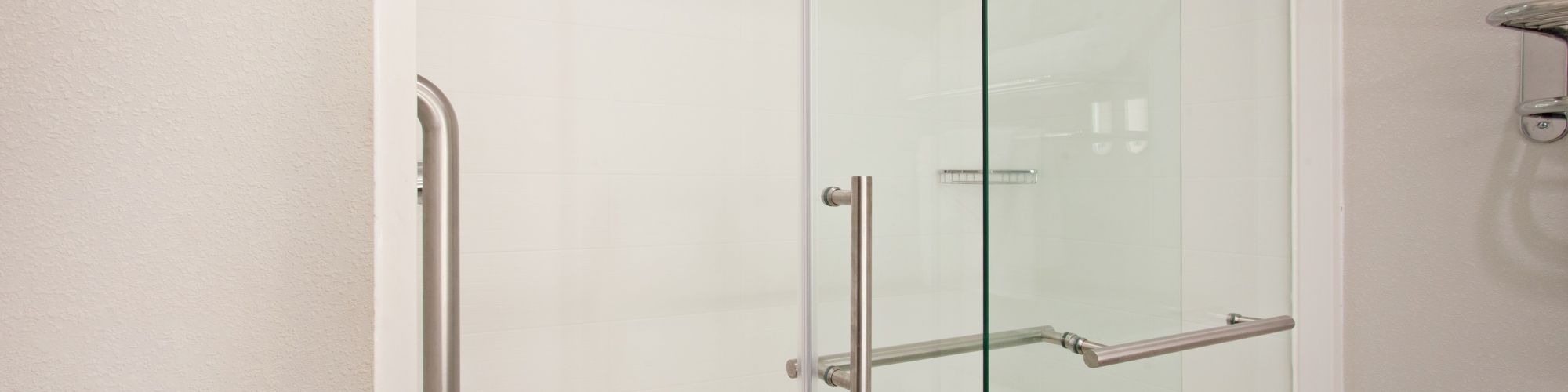 The image shows a modern shower with sliding glass doors and metal handles in a tiled bathroom. A towel rack is visible on the right side.