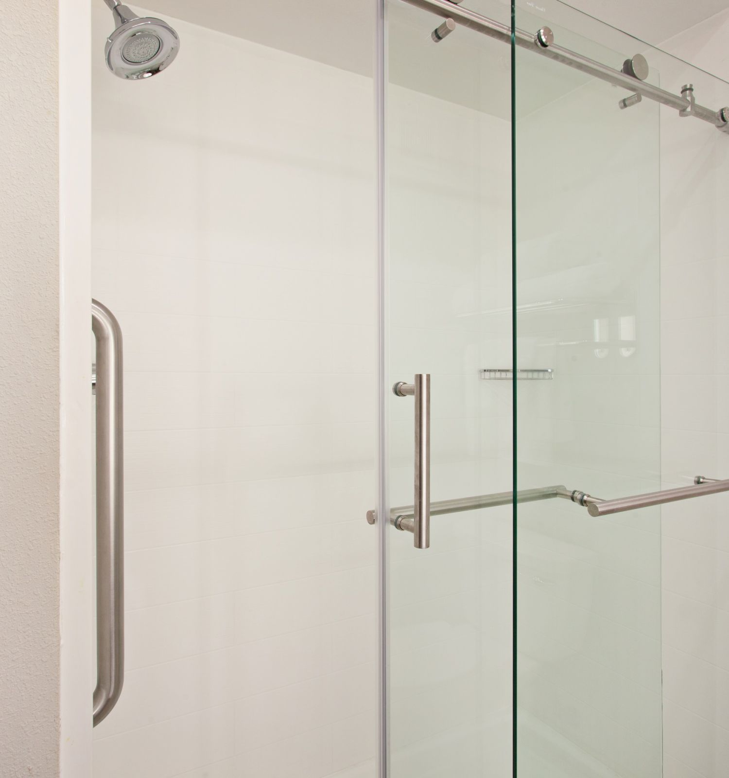 The image shows a modern glass shower enclosure with sliding doors and metal handles, featuring a wall-mounted showerhead and a clean, minimalistic design.