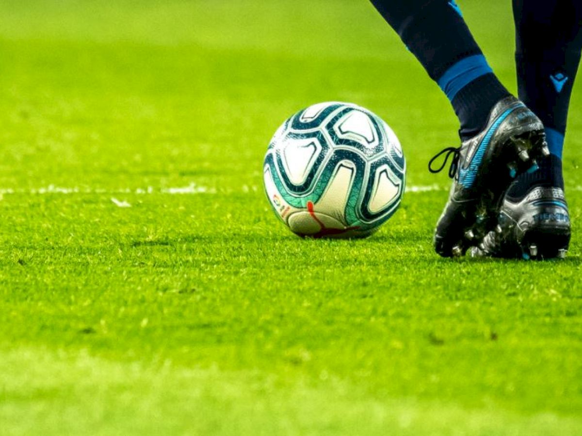 A soccer player, wearing blue and black cleats, is about to kick a soccer ball on a grass field.