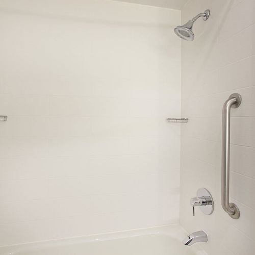 This image shows a white bathroom shower with a mounted showerhead, a grab bar, and a faucet. Two horizontal bars are also seen mounted to the wall.