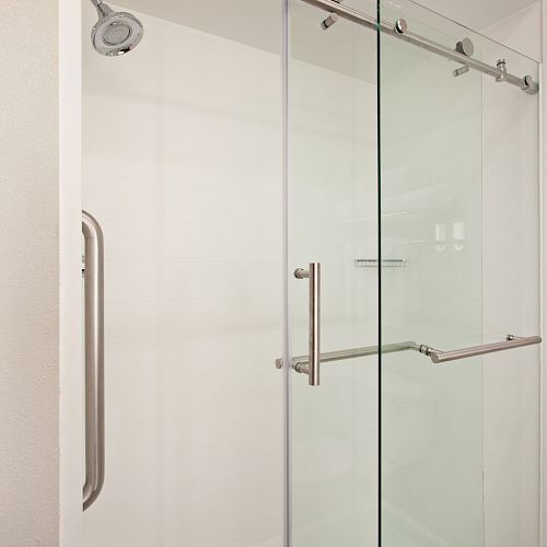 A modern shower with sliding glass doors, stainless steel handles, and a towel rack on the right side mounted on the wall.