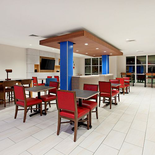 The image shows a modern dining area with red chairs and wooden tables, a coffee station on the right, and a TV mounted on the wall.