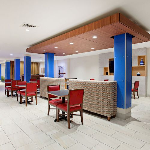 A modern dining area with tables, red chairs, blue columns, and cushioned booths, featuring clean white tile flooring and contemporary decor.