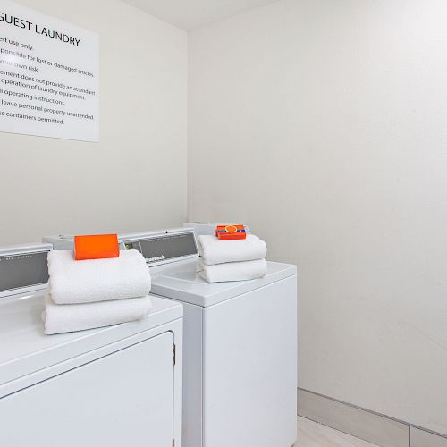 This image features a guest laundry room with a washer and dryer; each has folded towels on top. A sign with instructions is seen on the wall.