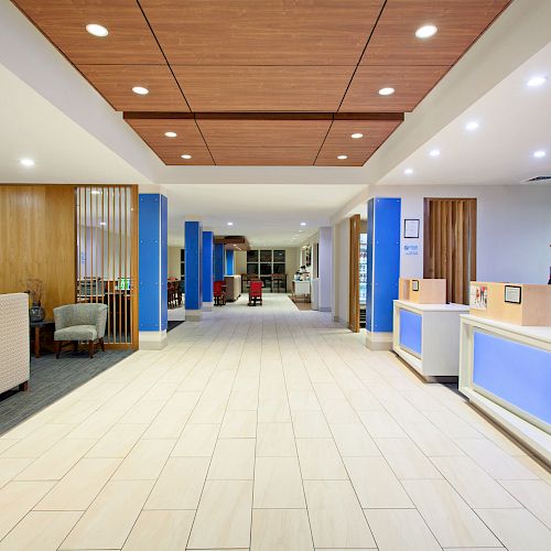 The image shows a modern lobby with blue accents, white tiled flooring, seating areas, and a reception desk on the right.