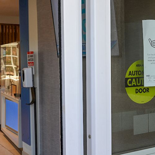 An indoor area with a sign stating mask policies is visible on a glass door, along with a yellow automatic door warning.