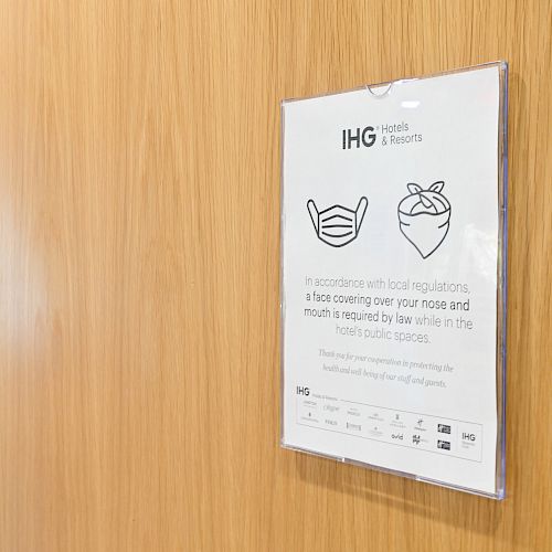 A sign on a wall indicating that face coverings are required by law, featuring icons of different mask types and the IHG Hotels & Resorts logo.