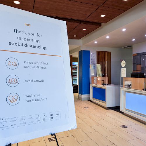 The image shows a signboard thanking people for respecting social distancing in a hotel lobby, with guidelines to keep 6 feet apart, avoid crowds, and wash hands regularly.