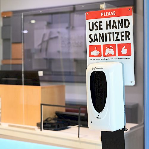 A hand sanitizer dispenser with a sign instructing to 