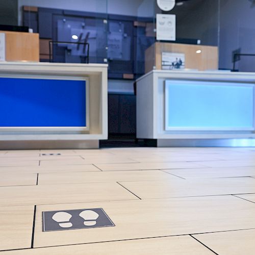 The image shows an empty service counter area with social distancing markers on the floor, indicating where to stand.