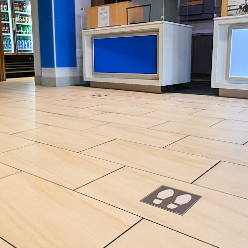 The image shows a tiled floor with markings to indicate where people should stand, likely for social distancing. There are counters in the background.