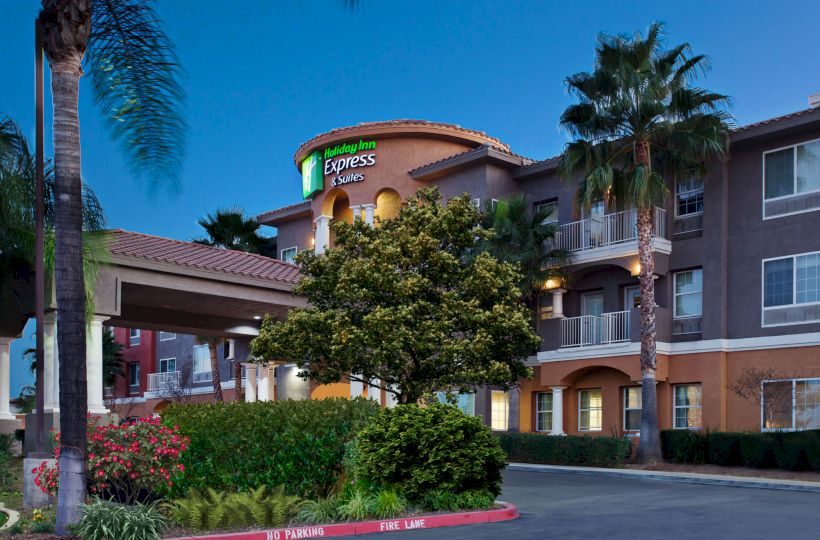 The image shows the exterior of a hotel building, identified as a Holiday Inn Express & Suites, surrounded by palm trees and greenery at dusk.