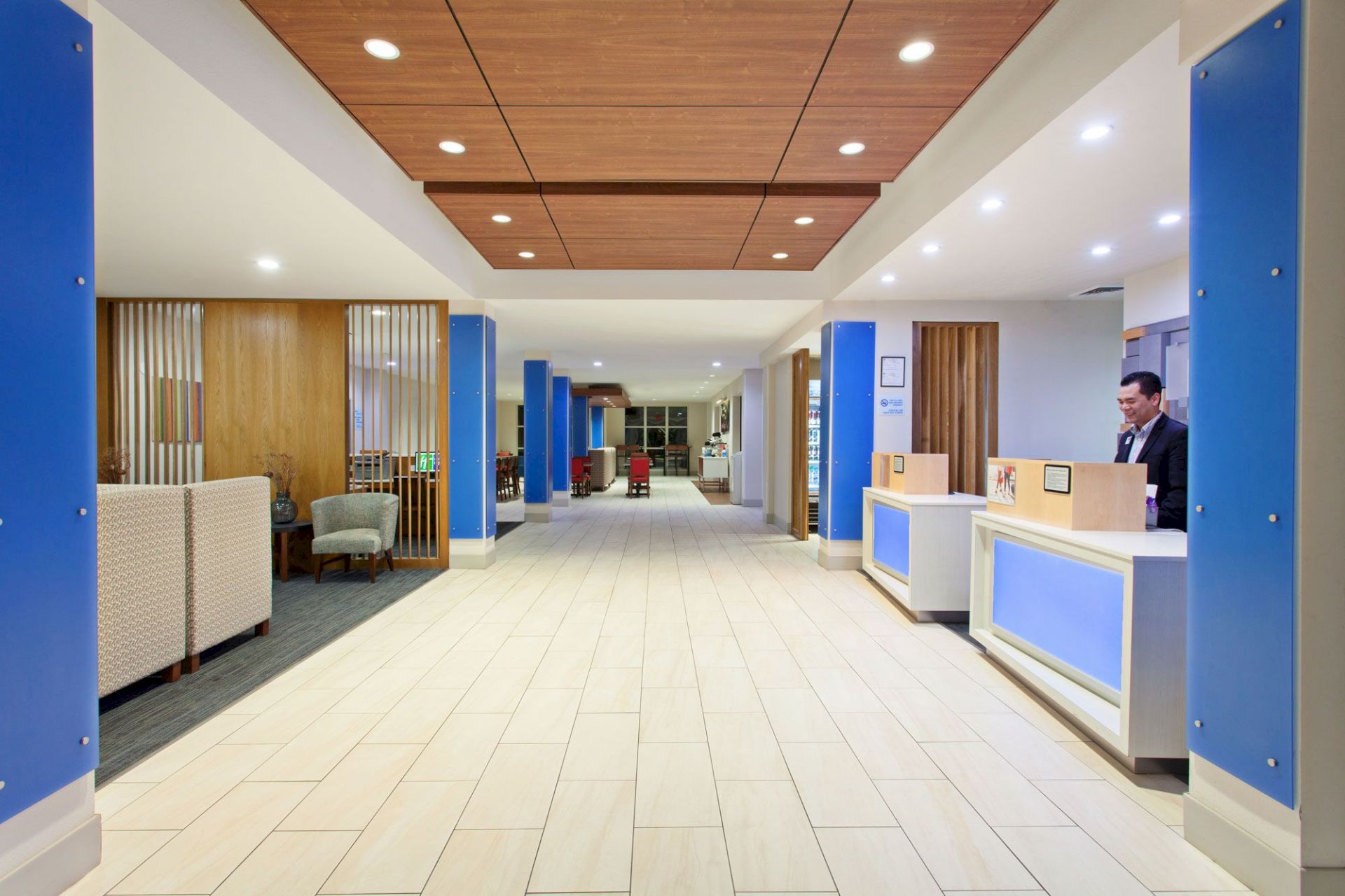 The image shows a modern reception area with seating on the left and a reception desk on the right, featuring blue and wooden accents.