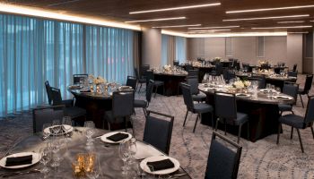 A banquet hall with round tables set with glassware, napkins, flowers, and candles, ready for an event.