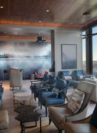 A modern lounge area with comfortable seating, large windows providing a scenic view of a waterfront and a Ferris wheel in the distance.