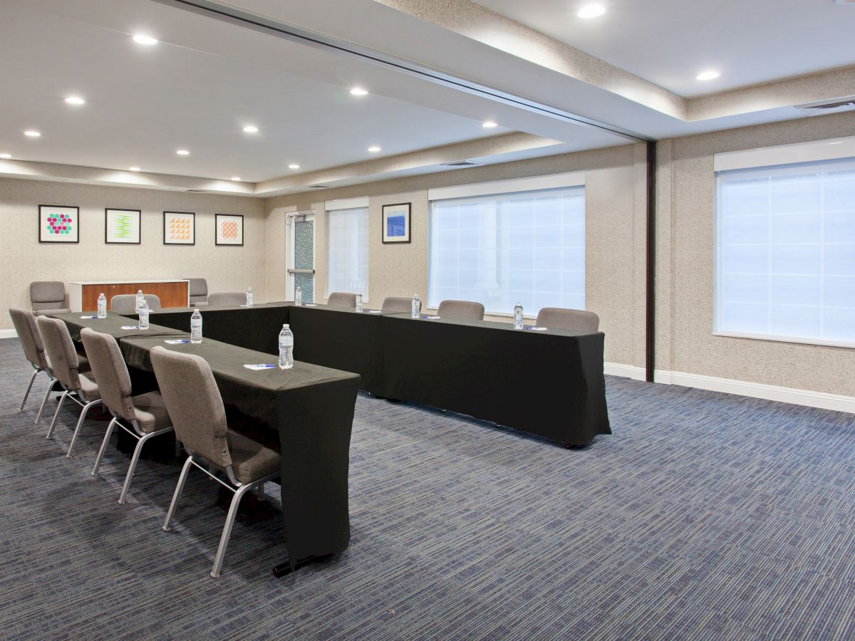 The image shows a conference room with chairs around a rectangular table, water bottles, and framed art on the walls, under bright ceiling lights.